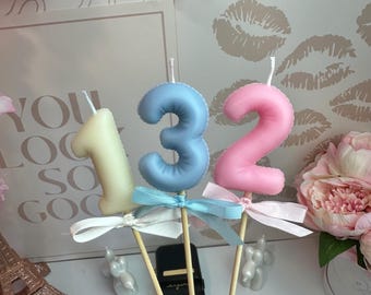 Puede incluir: Tres velas numéricas sobre palitos de madera, que incluyen un uno amarillo pálido, un tres azul claro y un dos rosa suave. Cada vela está adornada con un pequeño lazo de cinta de satén de color a juego atado en la base del número.
