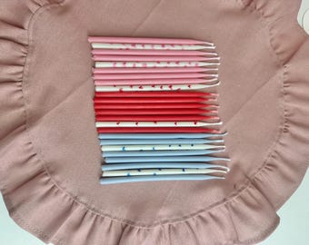 Puede incluir: Una colección de velas de cumpleaños en tonos rosa, rojo y azul, dispuestas sobre una tela rosa con volantes. Las velas están decoradas con corazones y lunares. Las velas miden aproximadamente 13 cm de largo.