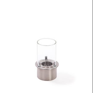 May include: A cylindrical tabletop fireplace featuring a brushed silver metal base and a clear glass chimney. The burner insert is made of stainless steel with a circular opening and a small metal wick component visible inside the glass enclosure.