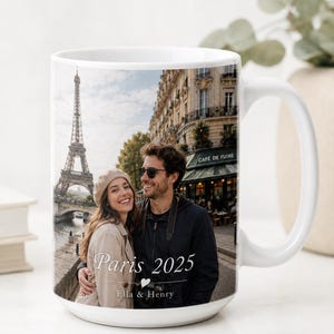 Peut inclure: Mug en c&eacute;ramique blanche avec une photo d'un couple &agrave; Paris, avec la Tour Eiffel en arri&egrave;re-plan. Le mug porte l'inscription "Paris 2025" et les noms "Ella & Henry".