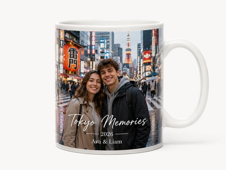 May include: White ceramic mug featuring a photograph of a couple in Tokyo, Japan. The mug has the text "Tokyo Memories 2026 Ava & Liam" in a handwritten style font. The background shows a busy street scene.
