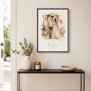 May include: A framed watercolor print of a couple kissing in front of a building. The print is in a black frame and is displayed on a black table with a vase, candle, and bowl. The print has the text "The Wilsons" and "Feb. 2022".