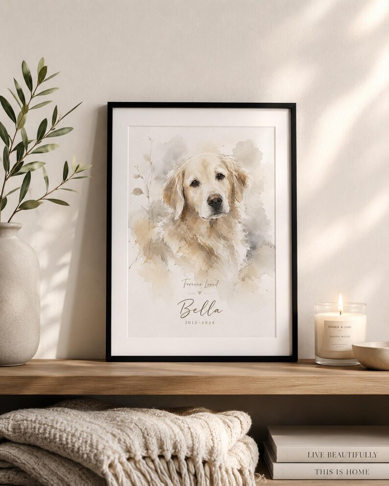 May include: A framed watercolor print of a Golden Retriever dog, with the name "Bella" and dates 2012-2024. The print is in a black frame and sits on a wooden shelf with a candle and a stack of books. The words "Forever Loved" are above the name.