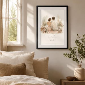 K&ouml;nnte beinhalten: Ein gerahmter Aquarelldruck mit einem Paar, das zusammen sitzt, mit dem Text "You and Me" sowie Namen und Datum darunter. Der Druck befindet sich in einem schwarzen Rahmen und h&auml;ngt an einer neutralfarbenen Wand &uuml;ber einem Bett mit beiger Bettw&auml;sche.