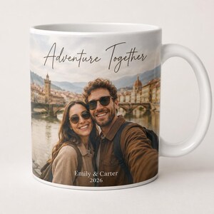 Pu&ograve; includere: Tazza in ceramica bianca con una fotografia di una coppia sorridente davanti a una citt&agrave; europea. La tazza ha le parole "Adventure Together" e i nomi "Emily & Carter 2026" stampati.