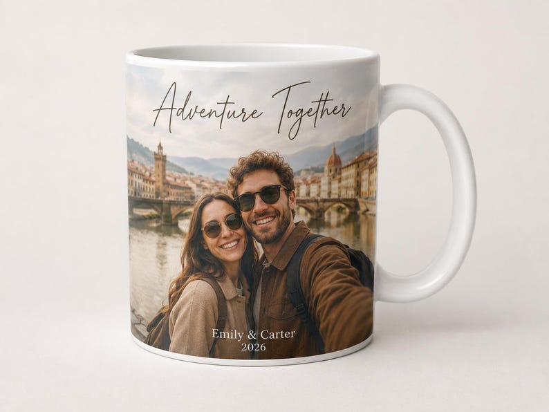 Pu&ograve; includere: Tazza in ceramica bianca con una fotografia di una coppia sorridente davanti a una citt&agrave; europea. La tazza ha le parole "Adventure Together" e i nomi "Emily & Carter 2026" stampati.