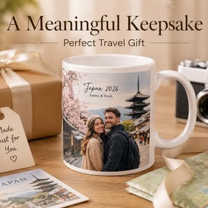 May include: White ceramic mug with a photo of a couple in Japan, a pagoda, and cherry blossoms. The mug has the text "Japan 2026 Emma & Noah." A gift box, tag, camera, and map are also in the image.