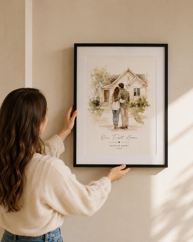 Puede incluir: Una impresi&oacute;n en acuarela enmarcada que representa a una pareja frente a una casa. La impresi&oacute;n tiene el texto "Our First Home" y los nombres "Chloe & Henry" con el a&ntilde;o 2024. El marco es negro.