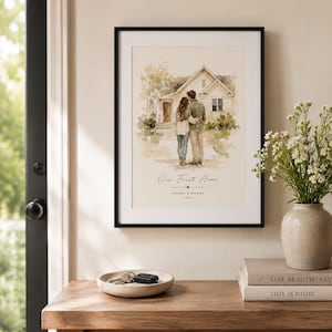 Puede incluir: Una impresi&oacute;n enmarcada con un marco negro, que representa a una pareja abraz&aacute;ndose frente a una casa. La impresi&oacute;n se titula "Our First Home" con nombres y un a&ntilde;o debajo. La impresi&oacute;n se exhibe sobre una mesa de madera con un cuenco decorativo y libros.