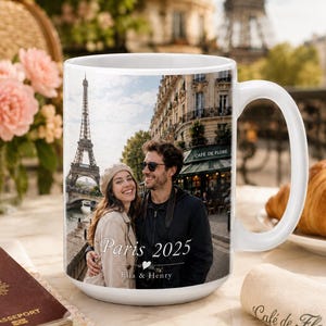 Peut inclure: Mug en c&eacute;ramique blanche avec une photo d'un couple &agrave; Paris, avec la Tour Eiffel en arri&egrave;re-plan. Le mug porte l'inscription "Paris 2025" et les noms "Ella & Henry". Une anse blanche est visible sur le c&ocirc;t&eacute; droit.