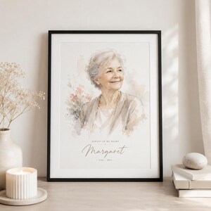 May include: A framed watercolor portrait of a smiling older woman, with the name "Margaret" and dates below. The portrait is in a black frame, with the text "Always in my heart". The image is displayed on a wooden surface.