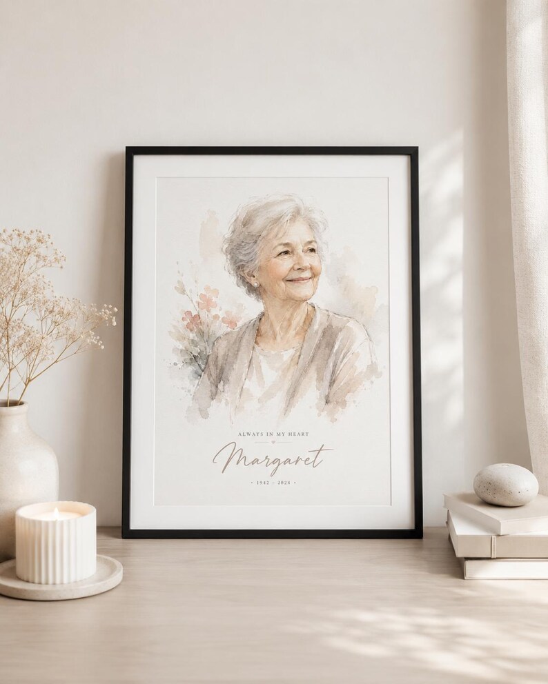 May include: A framed watercolor portrait of a smiling older woman, with the name "Margaret" and dates below. The portrait is in a black frame, with the text "Always in my heart". The image is displayed on a wooden surface.