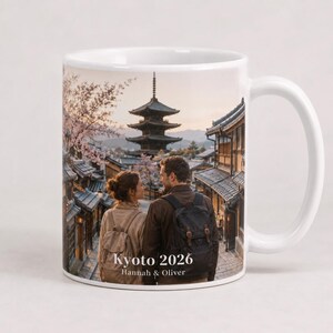 May include: White ceramic mug featuring a scenic image of Kyoto, Japan, with a pagoda and traditional buildings. The mug has a handle and includes the text "Kyoto 2026" and "Hannah & Oliver". The image shows a couple looking at each other.
