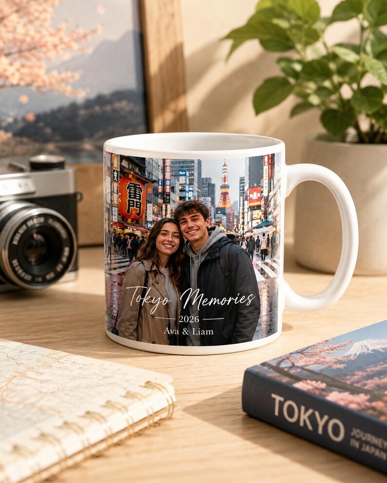 May include: White ceramic mug featuring a photograph of a couple in Tokyo, Japan, with the text "Tokyo Memories 2026 Ava & Liam." The mug has a large handle and is set on a wooden surface.