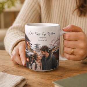 Puede incluir: Taza de cer&aacute;mica blanca con una fotograf&iacute;a de una pareja en Jap&oacute;n, con el texto "Our First Trip Together", "Japan 2026" y nombres. La taza tiene un asa curva y la sostiene una persona.