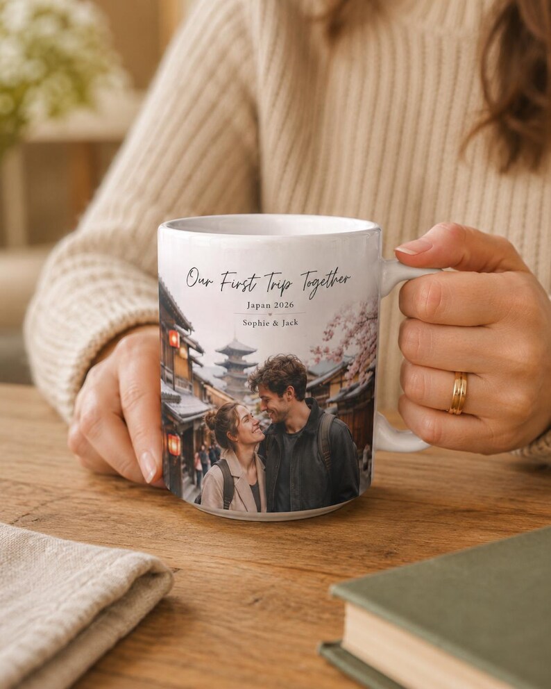 Puede incluir: Taza de cer&aacute;mica blanca con una fotograf&iacute;a de una pareja en Jap&oacute;n, con el texto "Our First Trip Together", "Japan 2026" y nombres. La taza tiene un asa curva y la sostiene una persona.