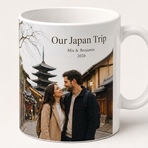 Pode incluir: Caneca de cer&acirc;mica branca com uma fotografia de um casal no Jap&atilde;o, com uma pagoda e edif&iacute;cios tradicionais ao fundo. O texto "Our Japan Trip" est&aacute; impresso acima dos nomes "Mia & Benjamin" e do ano "2026".