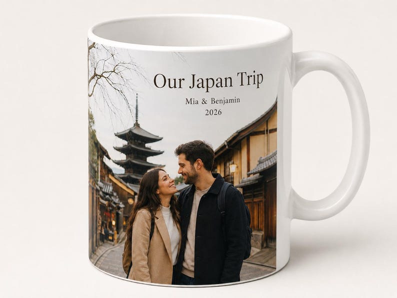 Pode incluir: Caneca de cer&acirc;mica branca com uma fotografia de um casal no Jap&atilde;o, com uma pagoda e edif&iacute;cios tradicionais ao fundo. O texto "Our Japan Trip" est&aacute; impresso acima dos nomes "Mia & Benjamin" e do ano "2026".
