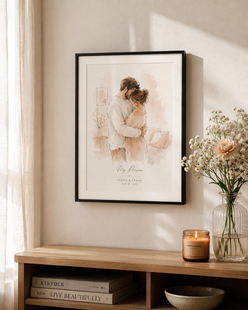 May include: A framed watercolor print featuring a couple embracing, with the text "My Person" and names below. The black framed art is displayed above a wooden console with books, a candle, and a vase of flowers.