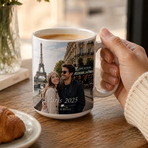 Peut inclure: Mug en c&eacute;ramique blanche avec une photo d'un couple &agrave; Paris, avec la Tour Eiffel en arri&egrave;re-plan. Le mug porte l'inscription "Paris 2025" et les noms "Ella & Henry". Le mug est rempli de caf&eacute;.