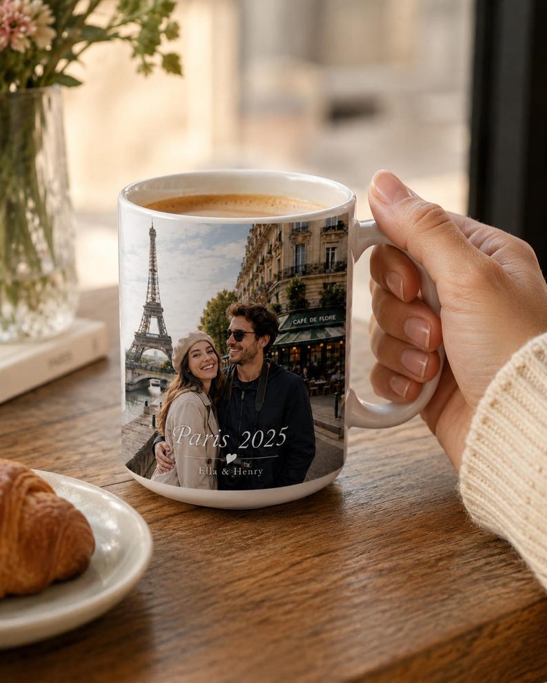 Peut inclure: Mug en c&eacute;ramique blanche avec une photo d'un couple &agrave; Paris, avec la Tour Eiffel en arri&egrave;re-plan. Le mug porte l'inscription "Paris 2025" et les noms "Ella & Henry". Le mug est rempli de caf&eacute;.