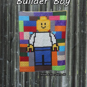 May include: A colorful quilt featuring a pixelated Lego-style figure of a smiling person wearing a white shirt and blue pants. The quilt is made up of squares of various colors, including red, orange, yellow, green, blue, purple, and gray. The quilt is labeled "Builder Boy" and has a finished size of 42 x 56 inches. Beginner.