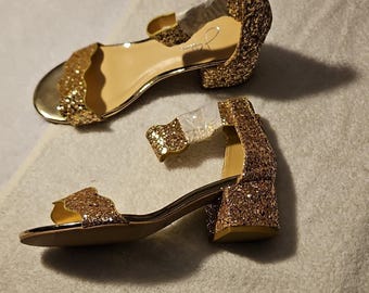 Sandalias sintéticas con purpurina dorada, tacón de bloque, tira en el tobillo, puntera abierta y cremallera. Talla 5.5.