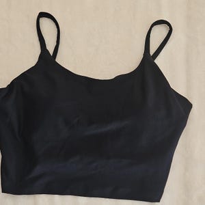 Può includere: Un top a camisole nero con sottili spalline. Il top ha una scollatura rotonda ed è realizzato in un tessuto liscio e lucido. Il capo è progettato per il comfort e lo stile, adatto per essere indossato a strati o da solo.