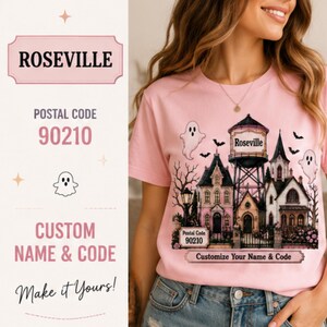 May include: A light pink t-shirt featuring a graphic of a haunted house, a water tower labelled ROSEVILLE, and ghosts. The design includes the text Postal Code 90210, Customize Your Name & Code, and Make it Yours. The shirt has short sleeves and a crew neck.