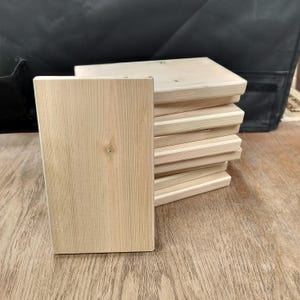 May include: A collection of unfinished wooden blocks, rectangular in shape. The blocks are a light colour, showing the wood grain. One block is standing upright in front of the stack. The blocks are ready for a woodworking project.