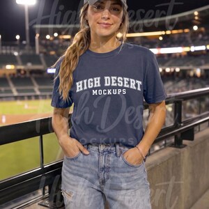 Peut inclure: Un t-shirt bleu marine &agrave; manches courtes avec le texte blanc "HIGH DESERT MOCKUPS" imprim&eacute; sur la poitrine dans une police universitaire, associ&eacute; &agrave; une casquette de baseball grise unie et un jean bleu clair avec des d&eacute;tails us&eacute;s.