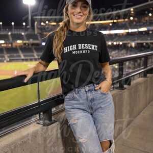 Peut inclure: Un t-shirt noir &agrave; manches courtes avec le texte blanc HIGH DESERT MOCKUPS imprim&eacute; sur la poitrine, associ&eacute; &agrave; une casquette de baseball grise et un jean en denim bleu clair us&eacute; avec des d&eacute;chirures aux genoux et aux cuisses.