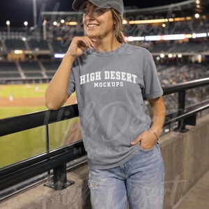Peut inclure: Un t-shirt gris &agrave; manches courtes avec le texte blanc HIGH DESERT MOCKUPS sur la poitrine, associ&eacute; &agrave; une casquette de baseball grise assortie et un jean en denim bleu clair us&eacute;. Le t-shirt a un col rond et une coupe d&eacute;contract&eacute;e.