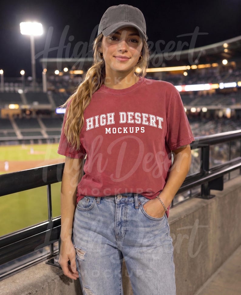 Peut inclure: Un t-shirt &agrave; manches courtes rouge fonc&eacute; avec le texte blanc HIGH DESERT MOCKUPS imprim&eacute; sur la poitrine, associ&eacute; &agrave; un jean bleu clair d&eacute;lav&eacute; et une casquette de baseball gris fonc&eacute;, port&eacute; dans un stade la nuit.