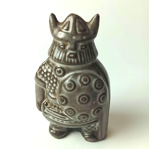 Può includere: Statuetta in ceramica marrone scuro di un guerriero vichingo. Indossa un elmo con corna e tiene uno scudo con motivi circolari. La statuetta ha un'armatura dettagliata ed è un oggetto decorativo. Misura circa 15 cm di altezza.