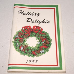 May include: A booklet titled "Holiday Delights" with a wreath illustration and the year 1992. The wreath features pinecones, red ribbon, and green foliage. The cover has a red and green border.