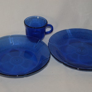 May include: A set of three blue glass dishes with a textured, floral design. The set includes a small cup, a medium bowl, and a large plate.