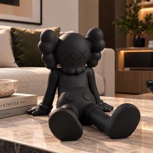 Puede incluir: Una figura coleccionable de color negro mate con cabeza redondeada, ojos en forma de cruz, orejas similares a huesos y manos enguantadas. El personaje está sentado con las piernas extendidas y viste pantalones cortos con dos botones circulares.