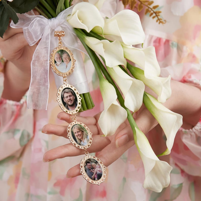 May include: A gold-toned metal photo charm pendant featuring four connected oval frames with ornate scalloped edges, each displaying a different photograph, attached to a white sheer ribbon tied around a bouquet of white calla lily flowers.