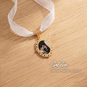 May include: An oval gold-toned pendant featuring an ornate filigree border and a central photograph of a couple. The pendant is suspended from a sheer white organza ribbon. The text Golden and ORGANZA RIBBON INCLUDED is visible.