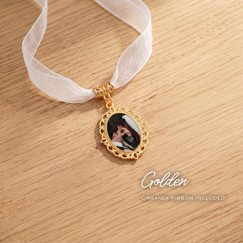 May include: An oval gold-toned pendant featuring an ornate filigree border and a central photograph of a couple. The pendant is suspended from a sheer white organza ribbon. The text Golden and ORGANZA RIBBON INCLUDED is visible.