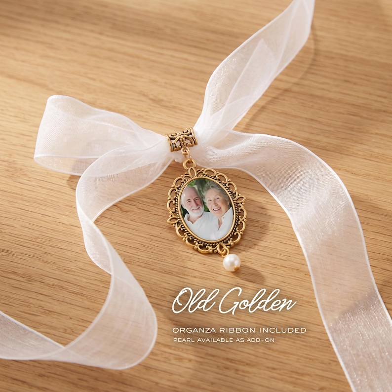 May include: An oval gold-toned pendant featuring a photograph of an older couple, suspended from a white organza ribbon. The pendant has an ornate filigree frame and a small dangling pearl at the bottom. Text on the image reads Old Golden.
