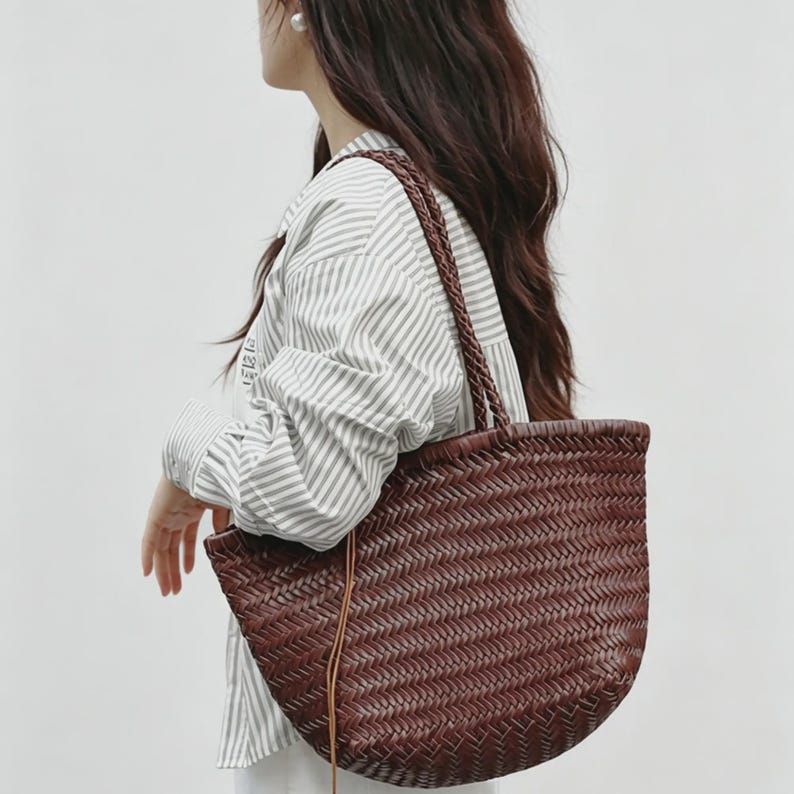 Peut inclure: Un sac fourre-tout marron tress&eacute; avec un fond arrondi et des anses tress&eacute;es. Le sac pr&eacute;sente un motif textur&eacute; et un d&eacute;tail de lani&egrave;re en cuir. Le sac est port&eacute; &agrave; l'&eacute;paule.