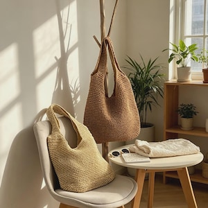 Puede incluir: Dos bolsos tote tejidos. Uno, de color beige claro, est&aacute; sobre una silla. El otro, marr&oacute;n oscuro, cuelga de un perchero de madera. Una peque&ntilde;a mesa tiene gafas de sol y un su&eacute;ter crema doblado.