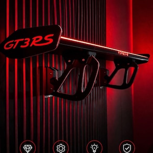 Könnte beinhalten: Ein schwarzes Wandregal in Form eines GT3RS-Heckflügels mit roter LED-Beleuchtung. Der Text GT3RS WANDREGAL, DESIGN PERFORMANCE PRÄZISION und JETZT ENTDECKEN ist sichtbar. Vier Symbole stehen für Premium-Design, hochwertige Verarbeitung, LED-Licht und Stabilität.