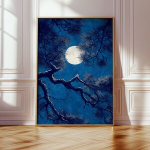 May include: A framed art print featuring a nighttime scene with a full moon and tree branches. The artwork has a blue background with a bright white moon and dark blue tree branches. The frame is a light gold color.