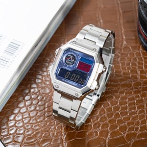 May include: A silver digital watch with a rectangular face and a stainless steel strap. The watch face shows the time, with the text "0:00:00" visible. The watch also features the text "10 YEAR BATTERY".
