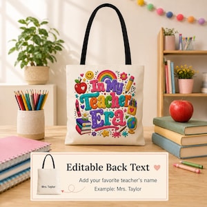 Puede incluir: Un bolso tote de color crema con asas negras que presenta un estampado gráfico colorido con el texto In My Teacher Era, rodeado de ilustraciones de un arcoíris, manzana, lápiz, libros y un globo terráqueo. Incluye texto editable en la parte posterior.