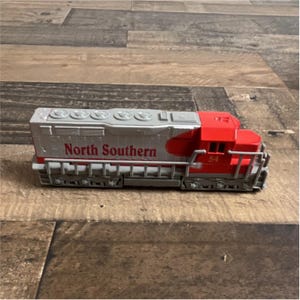 Op de afbeelding: Een speelgoedtreinlocomotief in rood en zilver. De woorden "North Southern" staan in het rood op de zijkant. Het nummer "54" staat in het wit op de voorkant van het rode gedeelte.