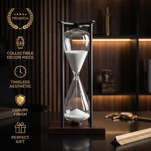 Può includere: Una clessidra con bulbi in vetro trasparente contenenti sabbia bianca, inserita in una cornice di metallo nero su una base in legno scuro. Il testo a sinistra recita: PREMIUM, COLLECTIBLE DECOR PIECE, TIMELESS AESTHETIC, LUXURY FINISH, PERFECT GIFT.